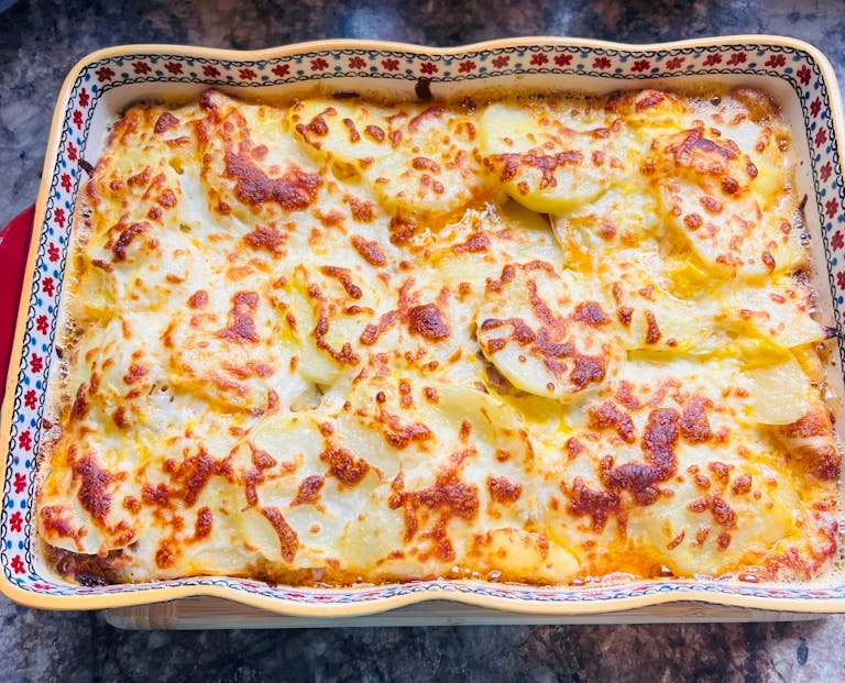 Delicious golden baked cheese and potato casserole in a decorative baking dish.