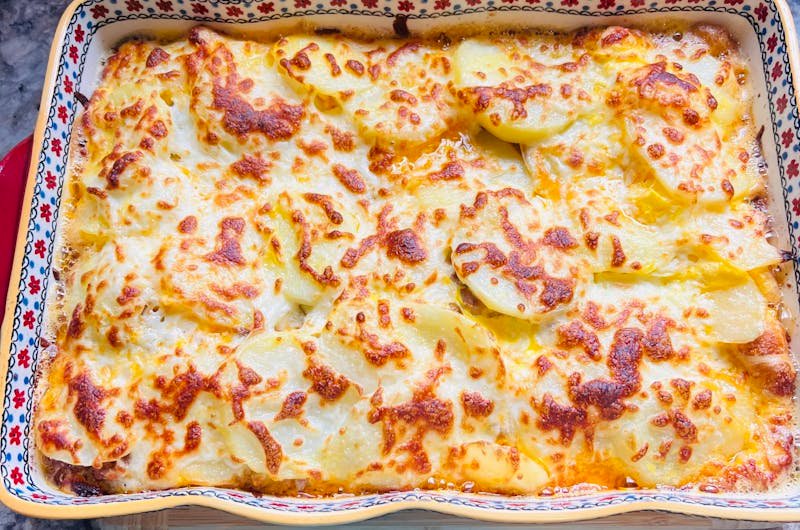 Delicious golden baked cheese and potato casserole in a decorative baking dish.
